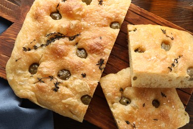 Photo of Pieces of delicious focaccia bread with olives and thyme on wooden table, top view