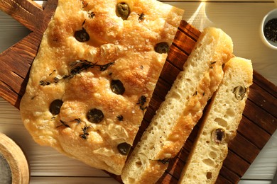 Photo of Pieces of delicious focaccia bread with olives, thyme and spices on white wooden table, flat lay