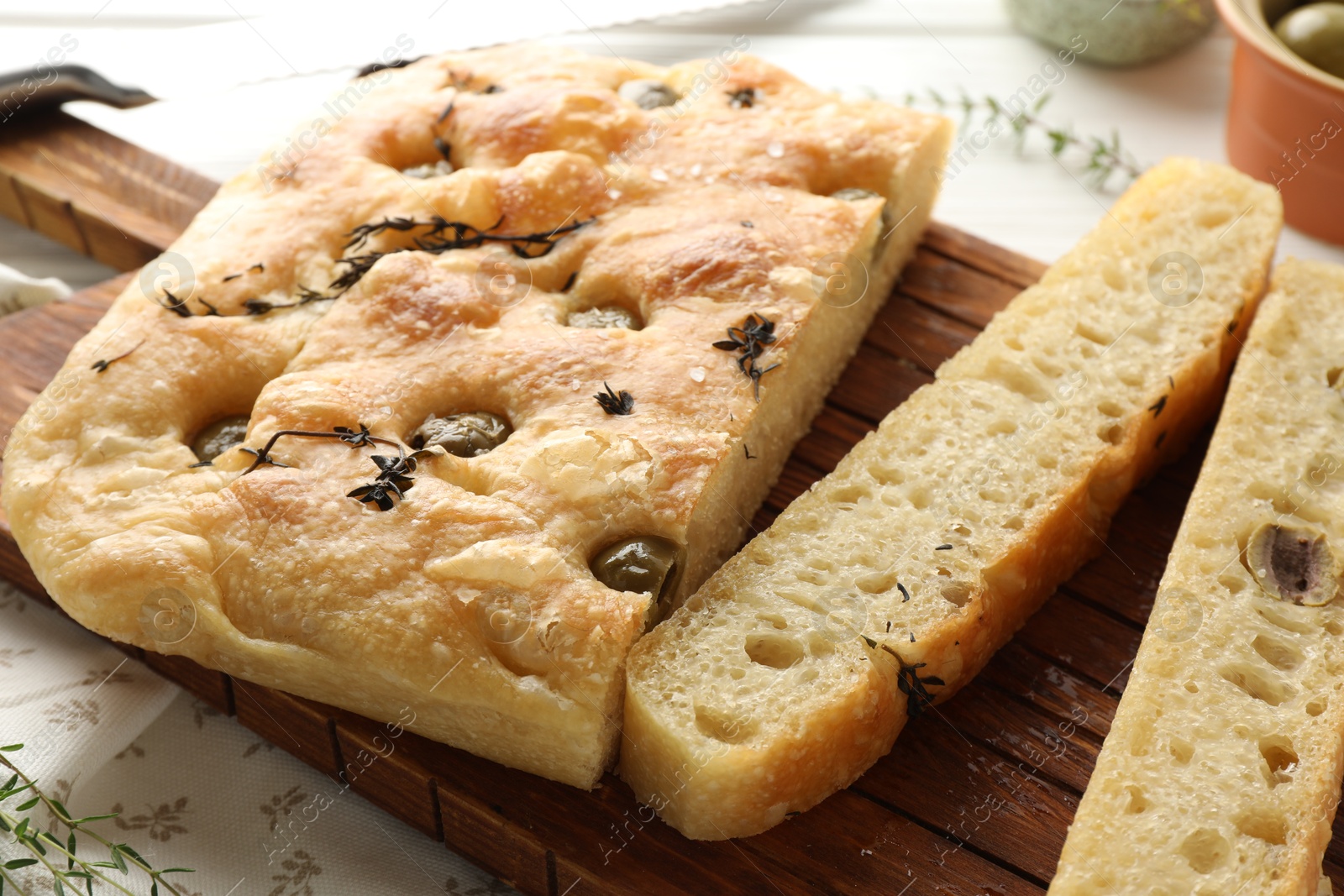 Photo of Pieces of delicious focaccia bread with olives, thyme and salt on table, closeup