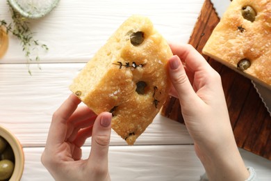 Photo of Woman with piece of delicious focaccia bread at white wooden table, top view