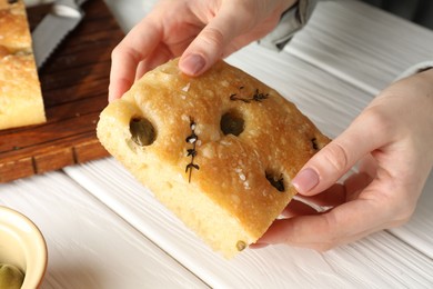 Photo of Woman with piece of delicious focaccia bread at white wooden table, closeup