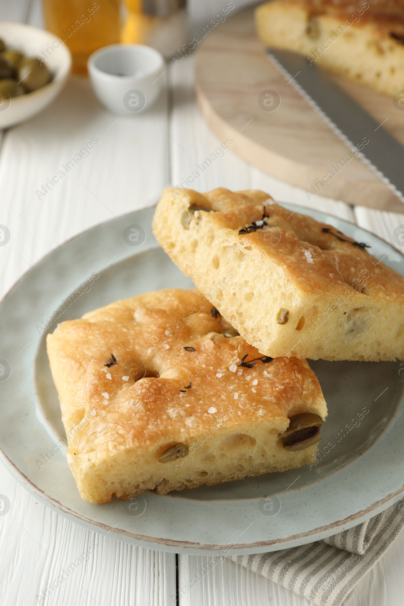 Photo of Pieces of delicious focaccia bread with olives, thyme and salt on white wooden table, closeup