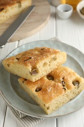 Photo of Pieces of delicious focaccia bread with olives, thyme, salt and knife on white wooden table, closeup