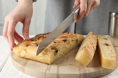 Photo of Woman cutting delicious focaccia bread at white wooden table, closeup