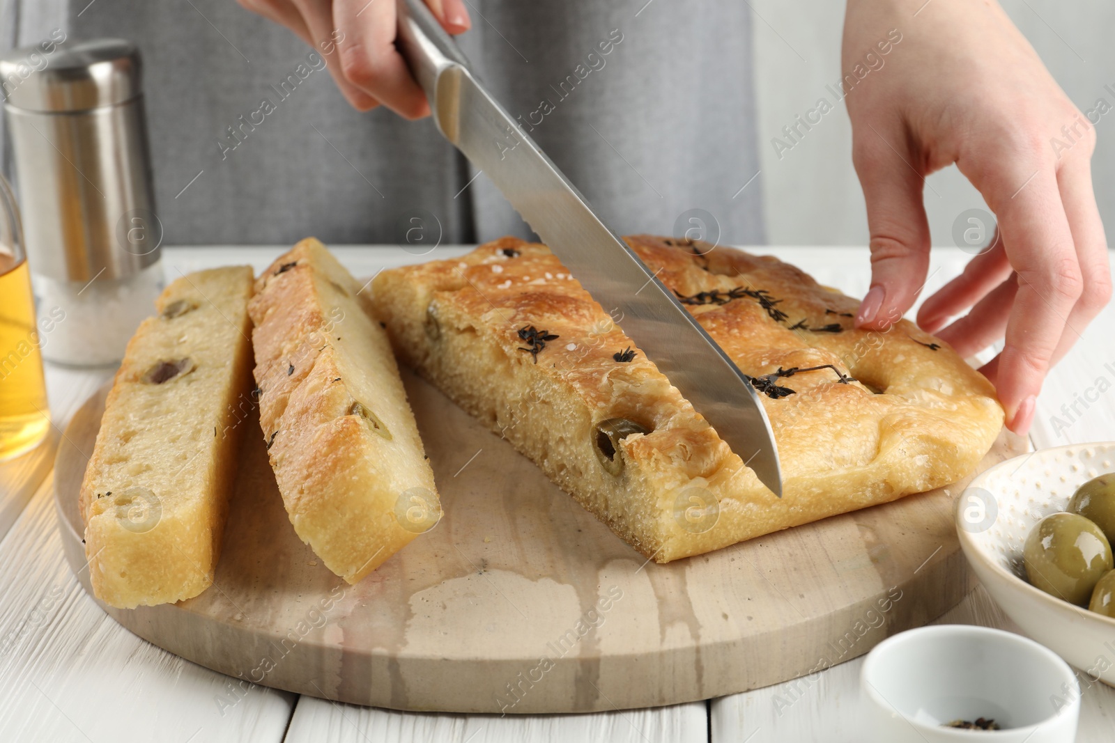 Photo of Woman cutting delicious focaccia bread at white wooden table, closeup