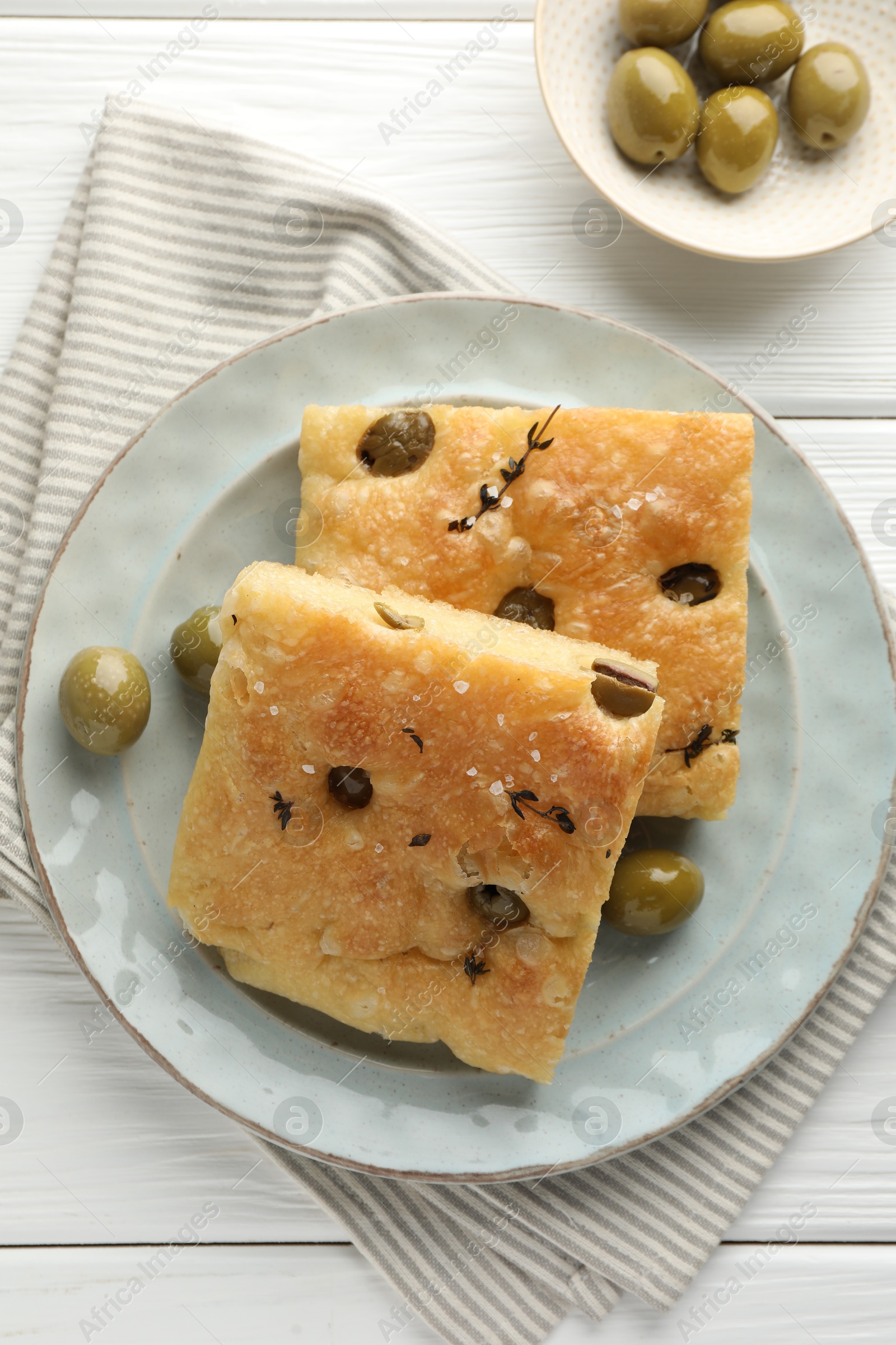 Photo of Slices of delicious focaccia bread with olives, thyme and salt on white wooden table, flat lay