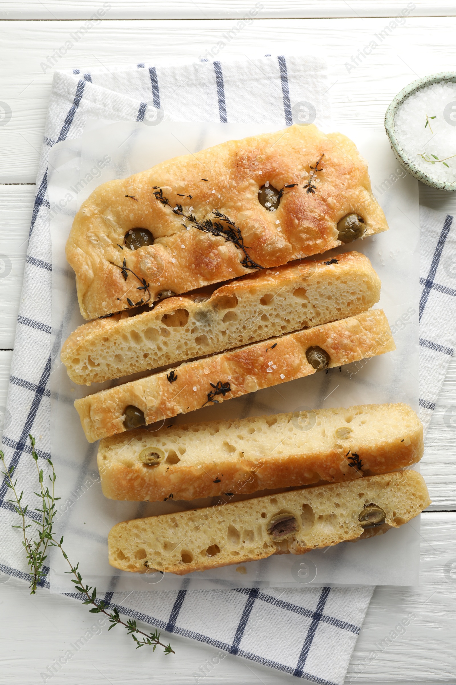 Photo of Slices of delicious focaccia bread with olives, thyme and salt on white wooden table, flat lay