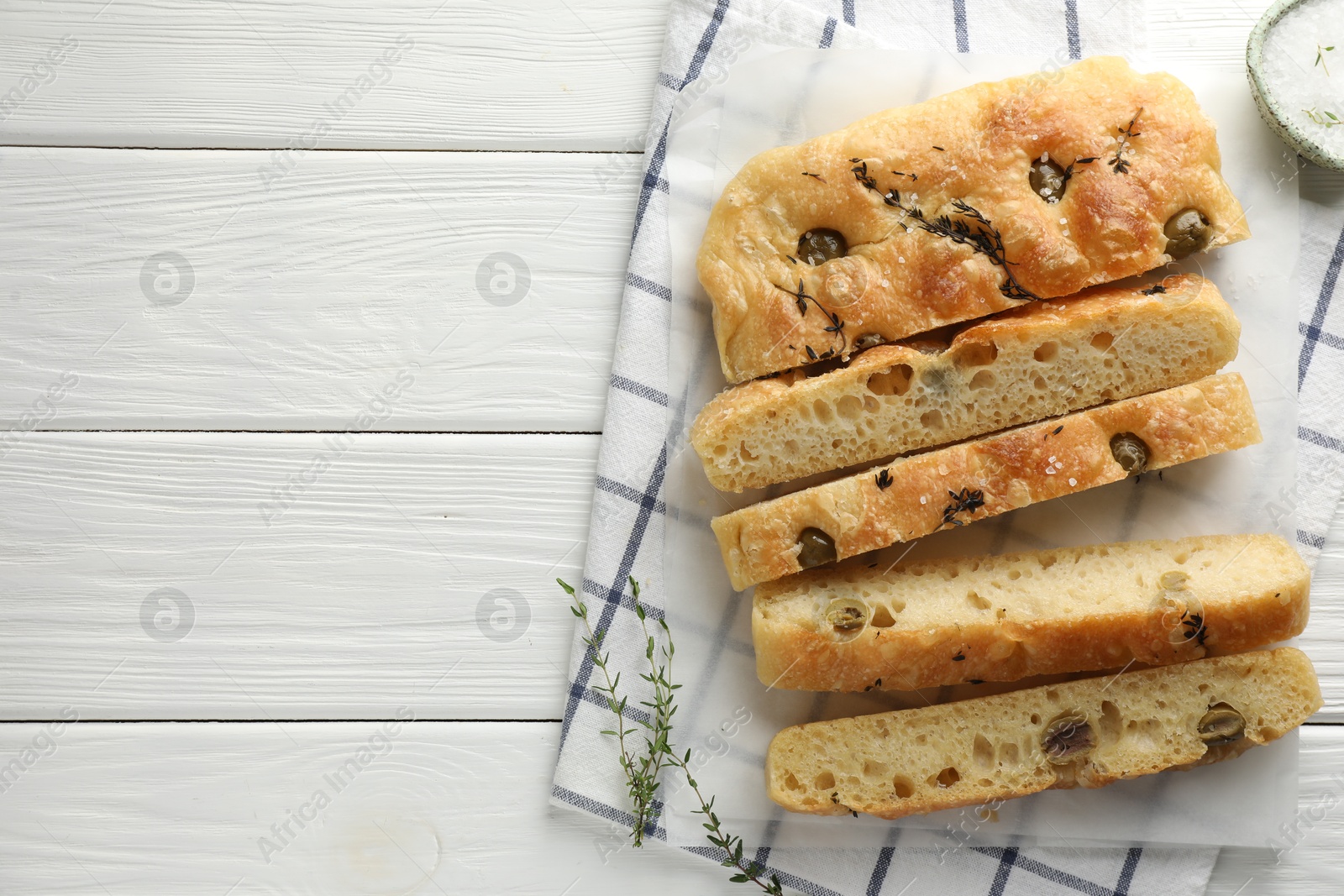 Photo of Slices of delicious focaccia bread with olives, thyme and salt on white wooden table, flat lay. Space for text