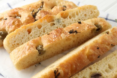 Photo of Slices of delicious focaccia bread with olives, thyme and salt on table, closeup