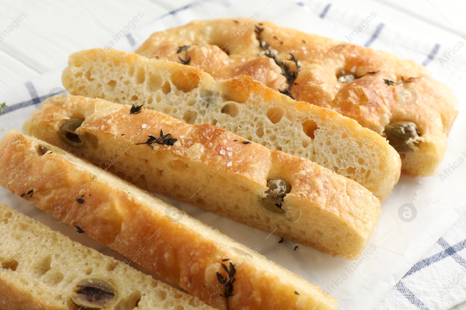 Photo of Slices of delicious focaccia bread with olives, thyme and salt on table, closeup