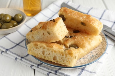 Photo of Slices of delicious focaccia bread with olives, thyme and salt on white wooden table, closeup