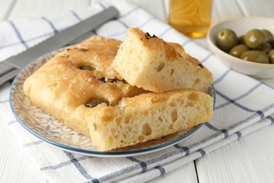 Photo of Slices of delicious focaccia bread with olives, thyme and salt on white wooden table, closeup