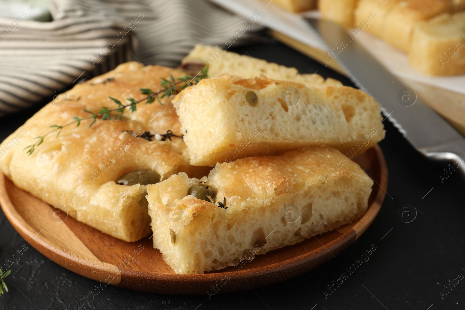 Photo of Slices of delicious focaccia bread with olives, thyme and salt on black table, closeup