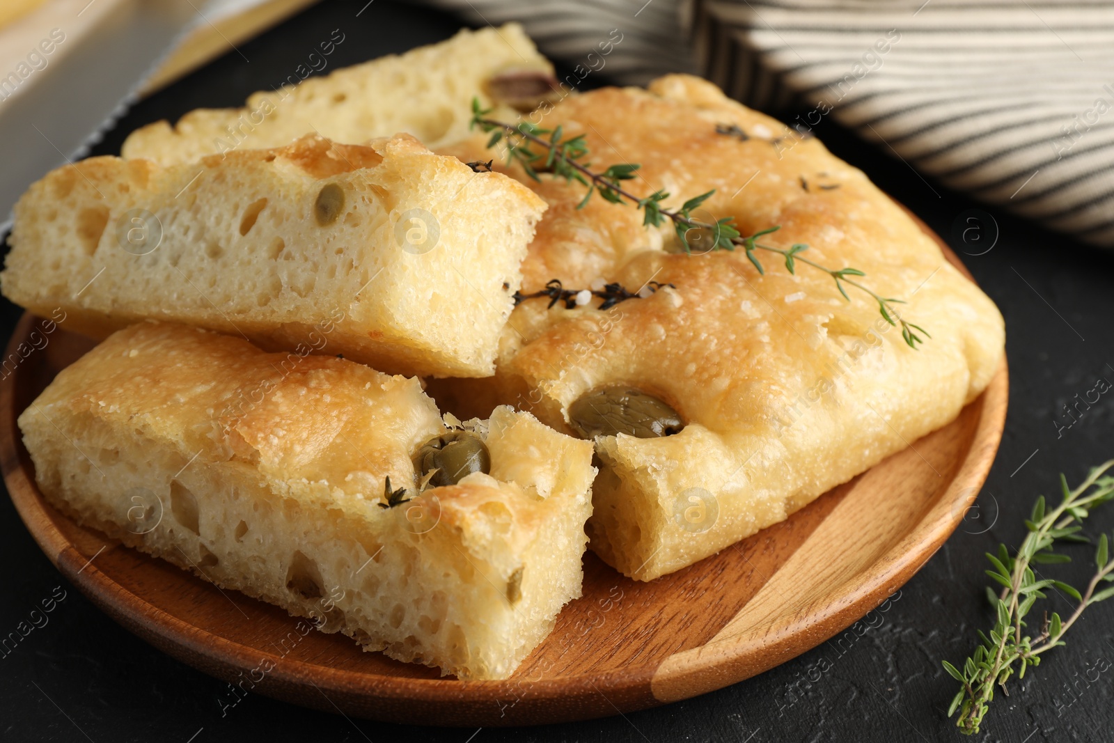 Photo of Slices of delicious focaccia bread with olives, thyme and salt on black table, closeup