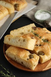 Photo of Slices of delicious focaccia bread with olives, thyme and salt on black table, closeup