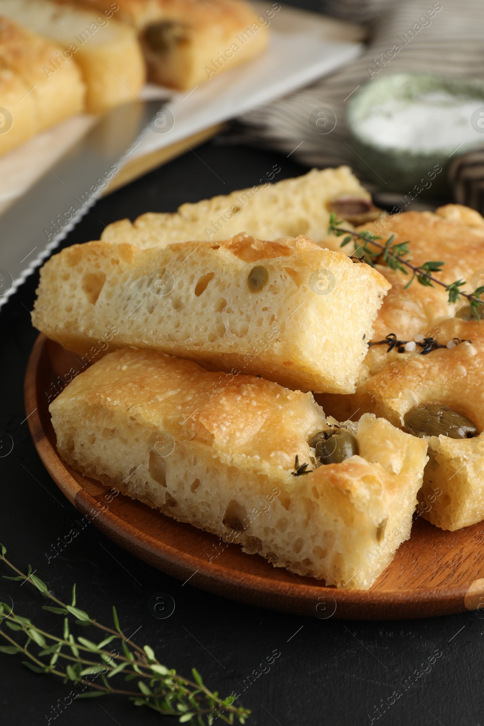 Photo of Slices of delicious focaccia bread with olives, thyme, salt and knife on black table, closeup