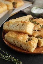 Photo of Slices of delicious focaccia bread with olives, thyme, salt and knife on black table, closeup