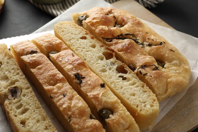 Photo of Slices of delicious focaccia bread with olives, thyme and salt on table, closeup