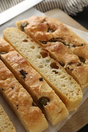 Photo of Slices of delicious focaccia bread with olives, thyme and salt on table, closeup