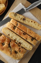 Photo of Slices of delicious focaccia bread with olives, thyme, salt and knife on black table, top view