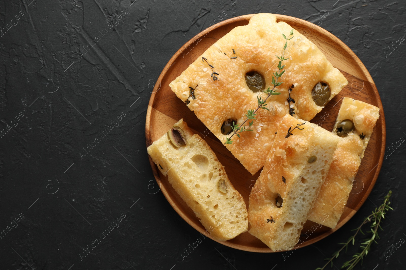 Photo of Slices of delicious focaccia bread with olives, thyme and salt on black table, top view. Space for text