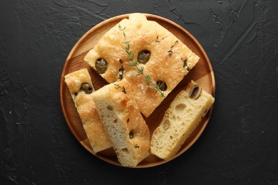 Photo of Slices of delicious focaccia bread with olives, thyme and salt on black table, top view