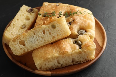 Photo of Slices of delicious focaccia bread with olives, thyme and salt on black table, closeup