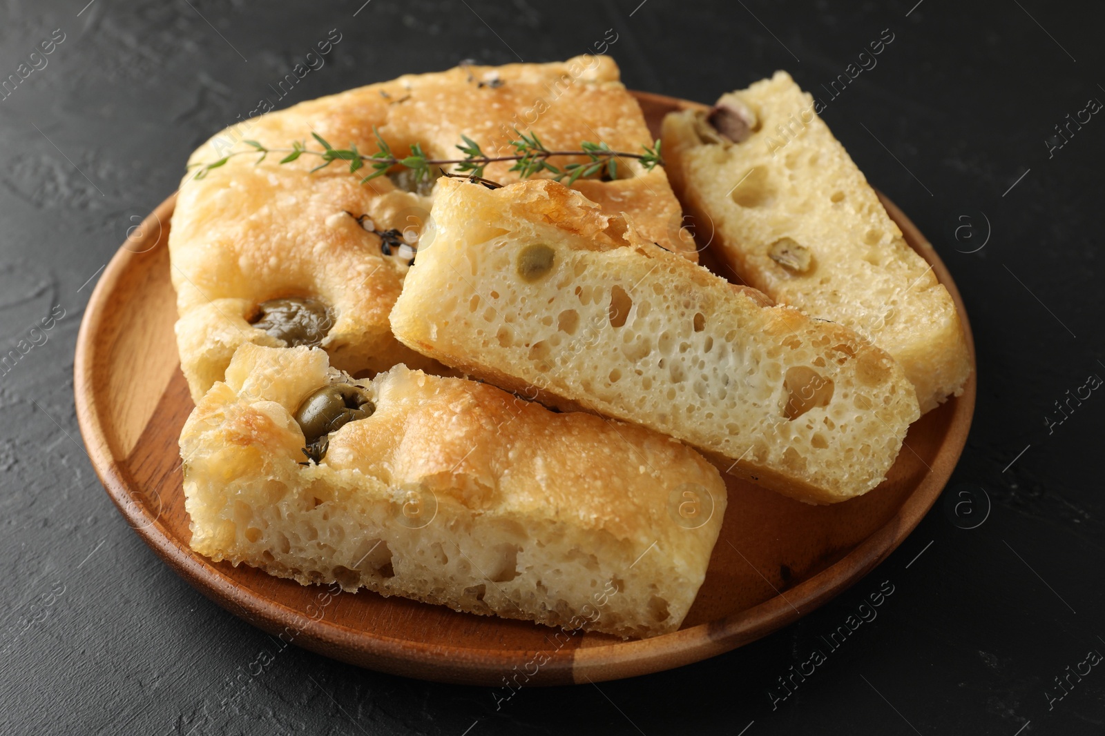 Photo of Slices of delicious focaccia bread with olives, thyme and salt on black table, closeup