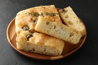 Photo of Slices of delicious focaccia bread with olives, thyme and salt on black table, closeup