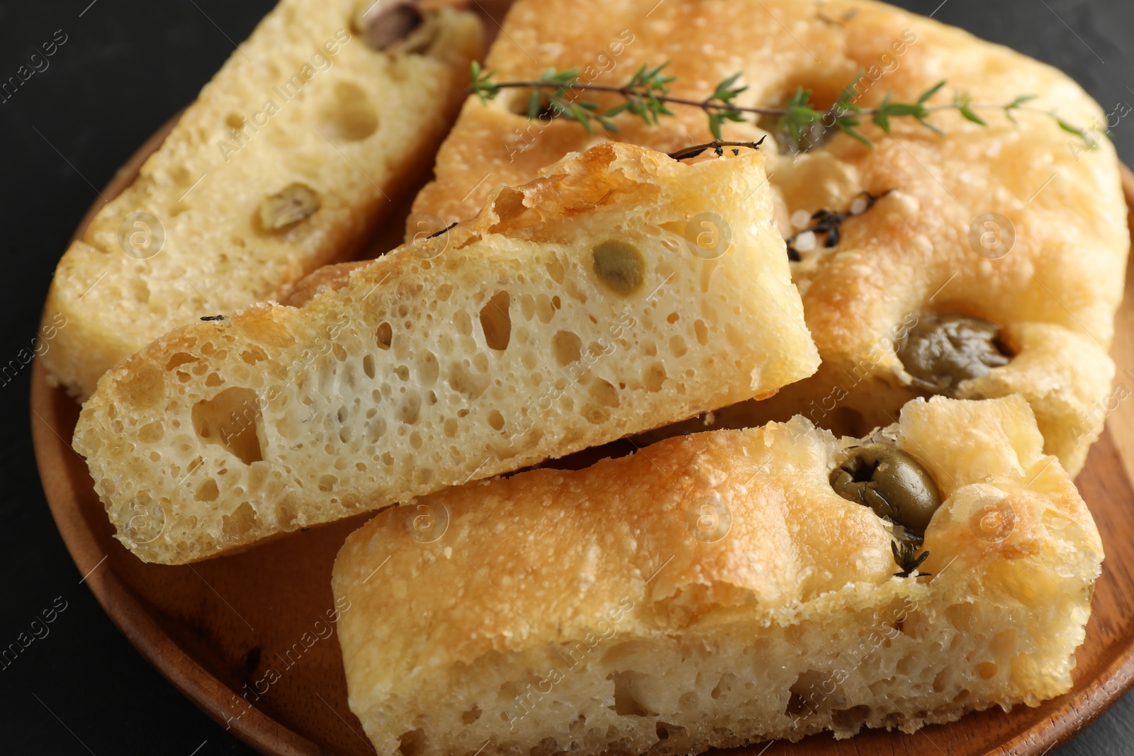 Photo of Slices of delicious focaccia bread with olives, thyme and salt on table, closeup