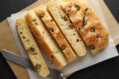 Photo of Slices of delicious focaccia bread with olives, thyme, salt and knife on black table, top view