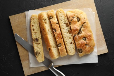 Photo of Slices of delicious focaccia bread with olives, thyme, salt and knife on black table, top view