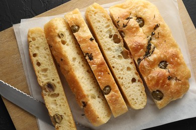 Photo of Slices of delicious focaccia bread with olives, thyme, salt and knife on black table, top view