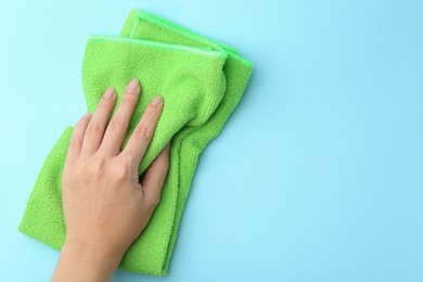 Photo of Woman with clean green microfiber cloth on light blue background, top view. Space for text