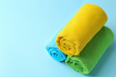 Photo of Rolled different microfiber cloths on light blue background, closeup. Space for text