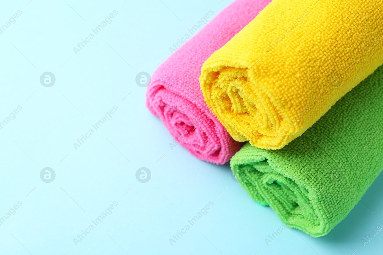 Photo of Rolled different microfiber cloths on light blue background. Space for text