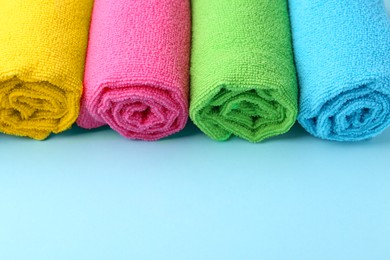 Photo of Rolled different microfiber cloths on light blue background, closeup