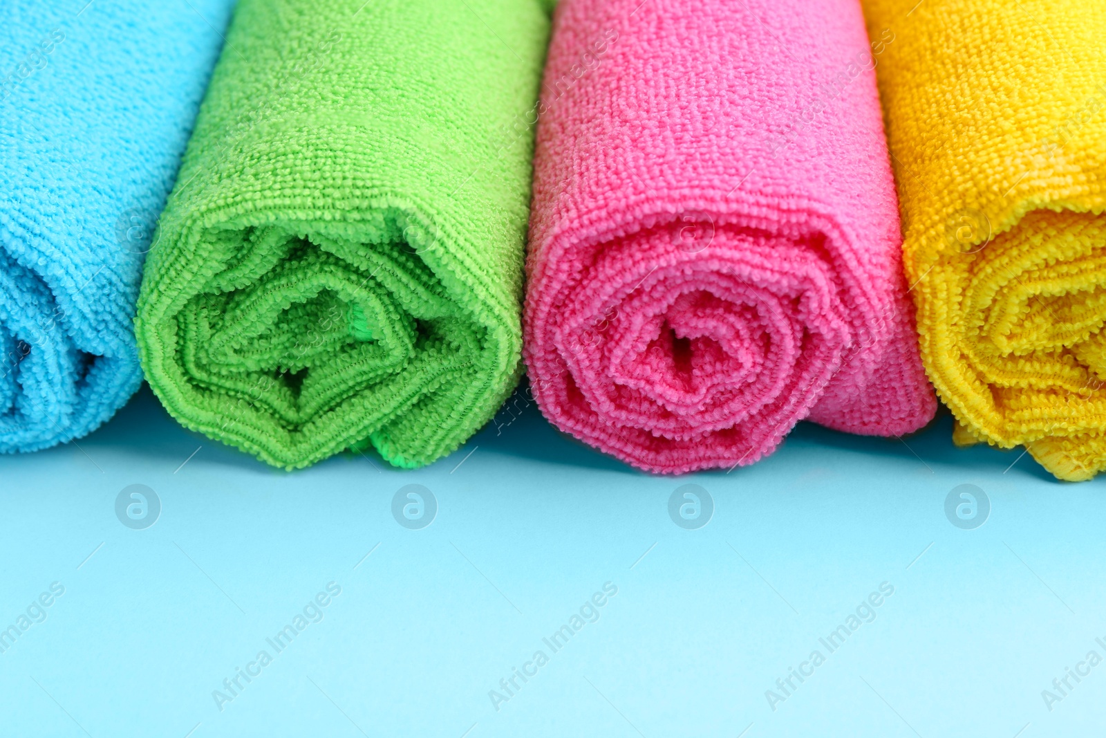 Photo of Rolled different microfiber cloths on light blue background, closeup