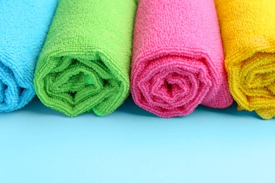 Photo of Rolled different microfiber cloths on light blue background, closeup