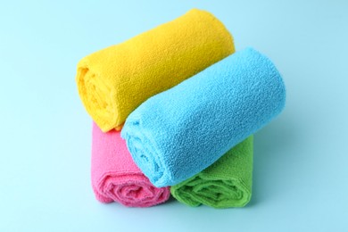 Photo of Rolled different microfiber cloths on light blue background, closeup