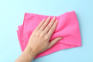 Photo of Woman with clean pink microfiber cloth on light blue background, top view