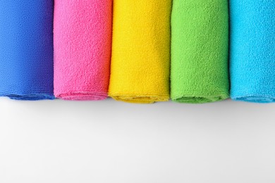 Photo of Rolled different microfiber cloths on white background, top view. Space for text