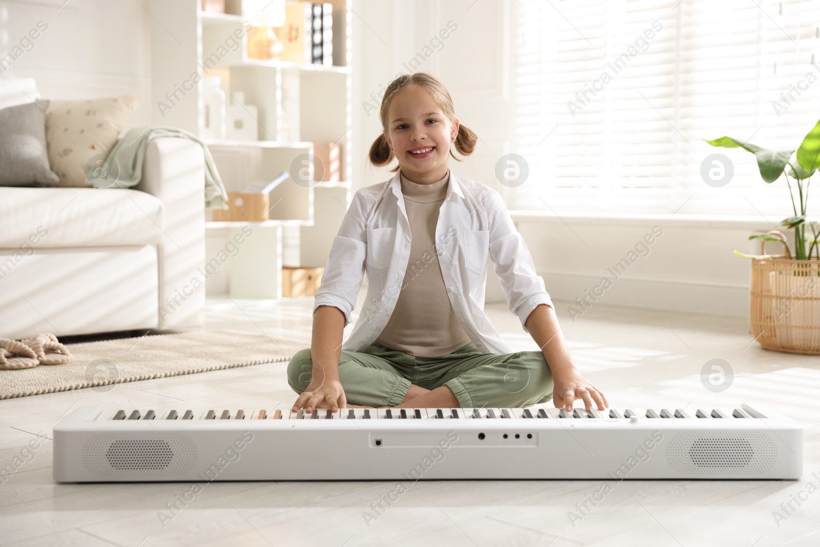 Photo of Cute girl playing synthesizer on floor at home