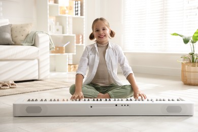 Cute girl playing synthesizer on floor at home