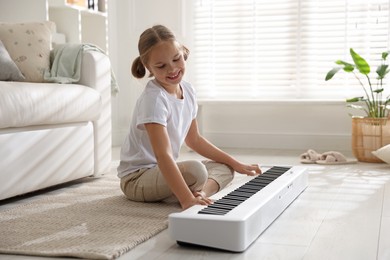 Photo of Cute girl playing synthesizer on floor at home