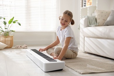 Cute girl playing synthesizer on floor at home