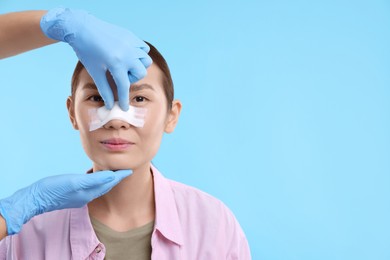 Photo of Doctor checking patient's nose after plastic surgery operation on light blue background, closeup. Space for text