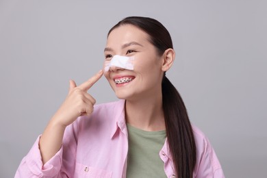 Photo of Woman with medical bandage on her nose after plastic surgery operation against light grey background