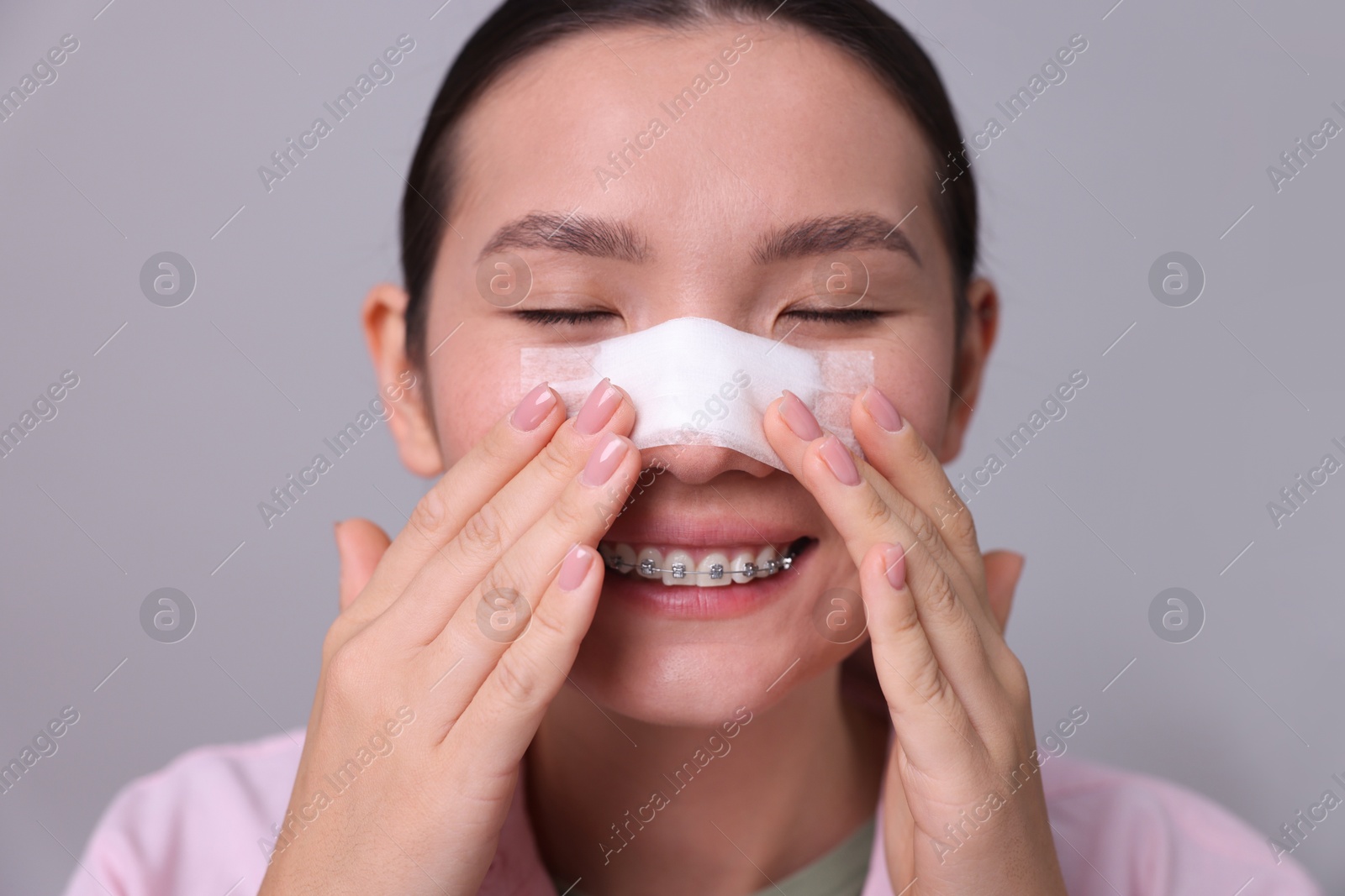 Photo of Woman with medical bandage on her nose after plastic surgery operation against light grey background, closeup