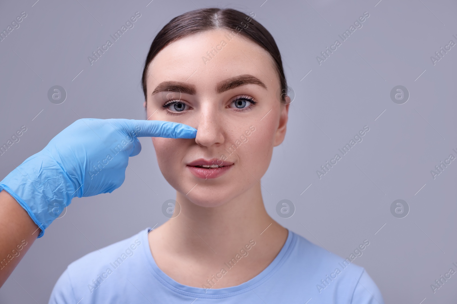 Photo of Doctor checking patient's nose before plastic surgery operation on grey background, closeup